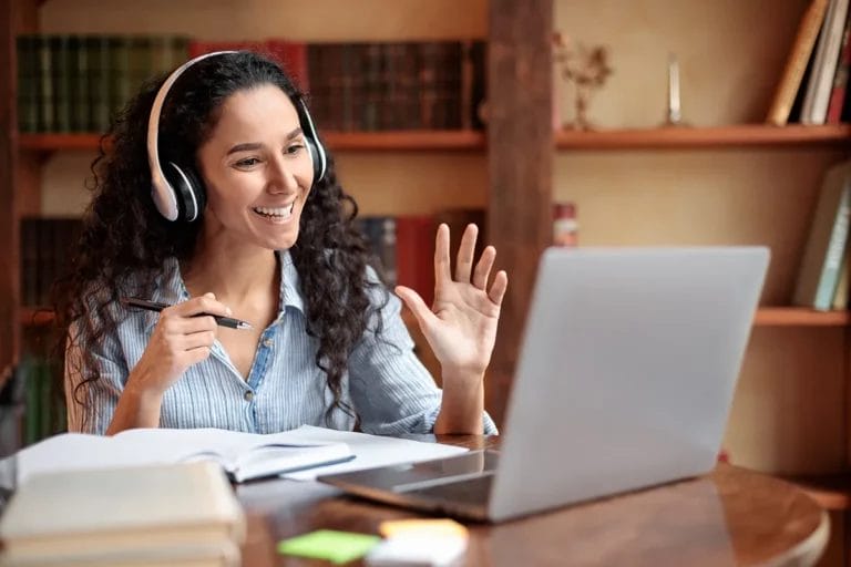 A remote tutor wearing headphones and using a laptop to conduct her session.