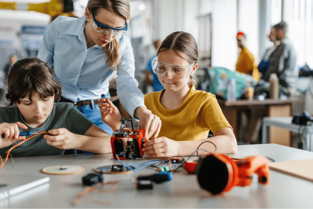 Teacher instructs two students in robotics engineering classroom