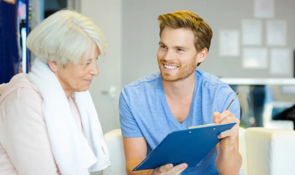 Smiling trainer reviews paperwork on a clipboard with senior client.