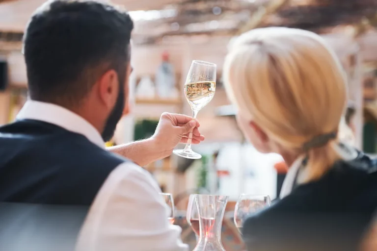 Two professional cavists study the characteristics of white wine in a glass at a trade expo.