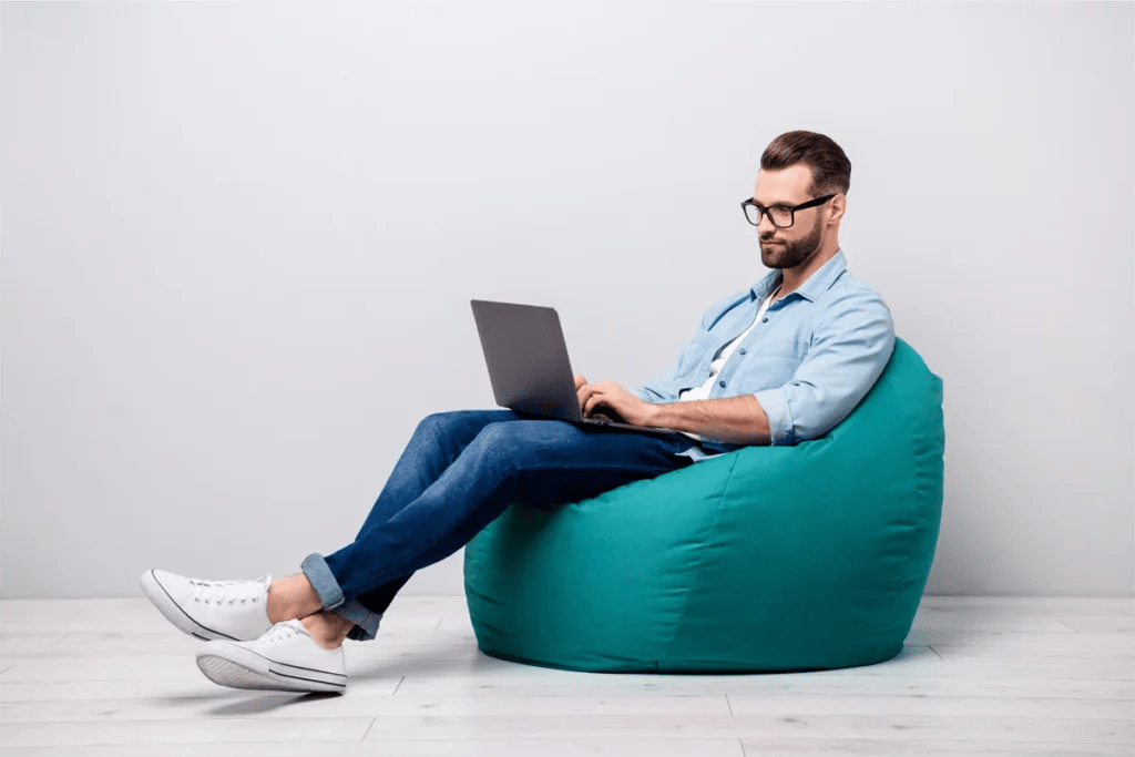 A man on a bean bag researches insurance on his computer.