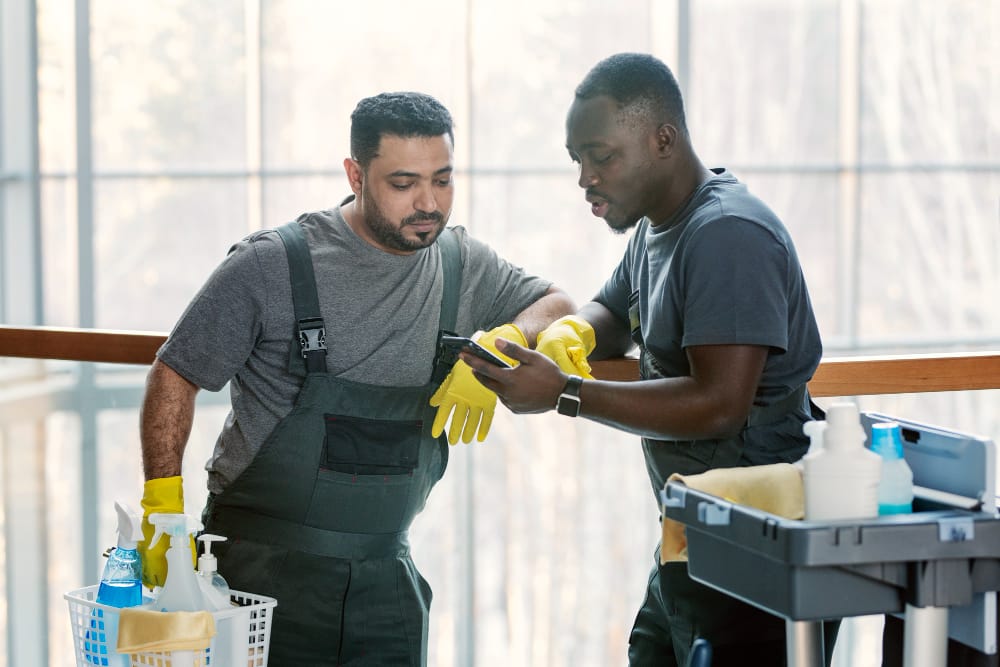 two men in cleaning uniforms looking at a phone