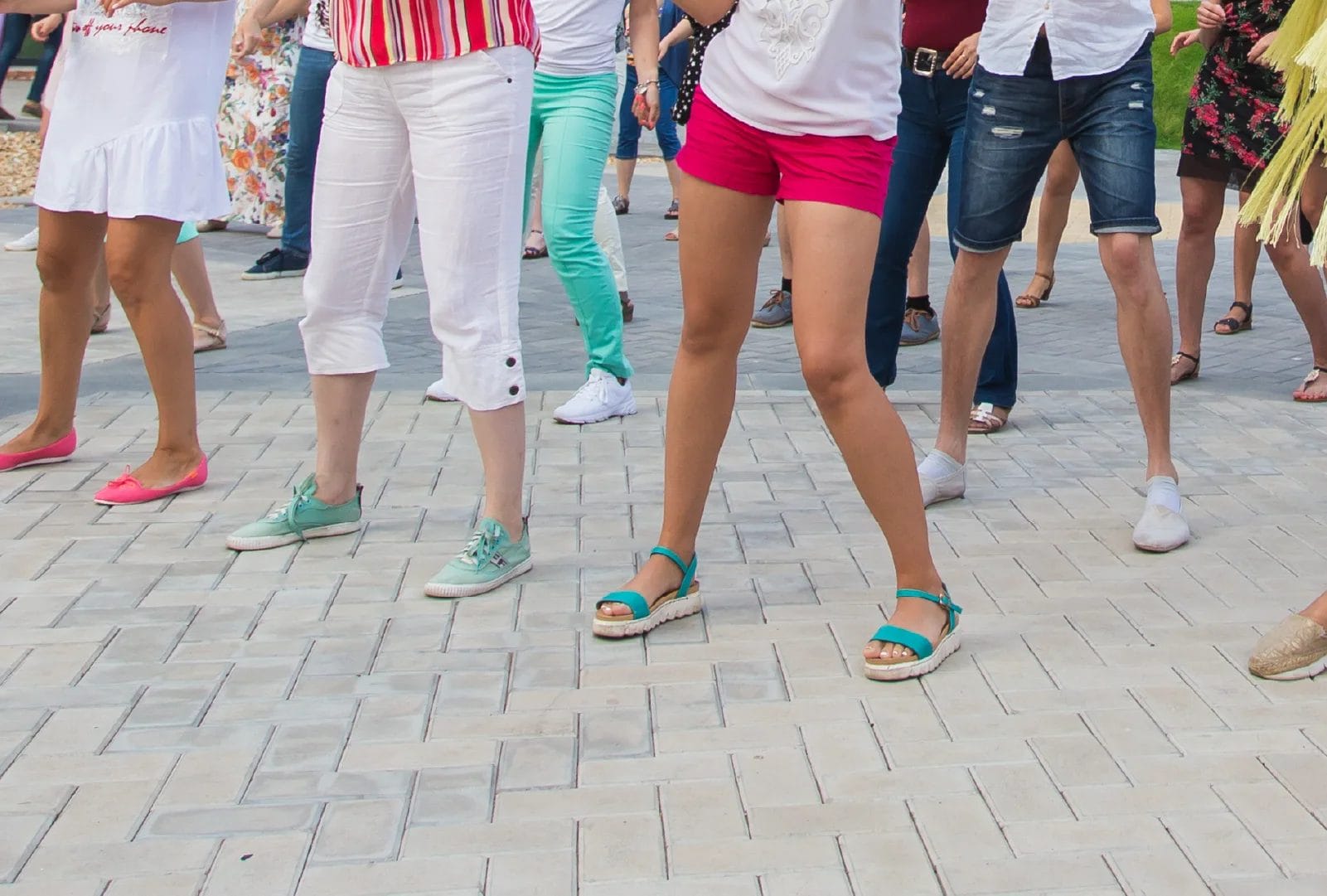 An image of the lower half of a group of dancers wearing colorful clothes as they dance outside.
