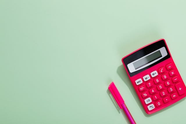 a red calculator and pen against a green background