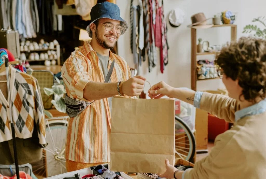 A pop-up shop owner is happily handing a bag of products to a customer.