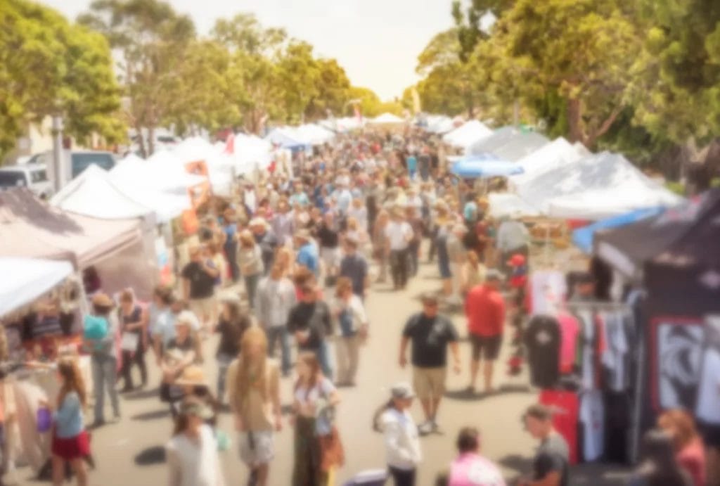 A blurry crowd attending a street market lined with vendors.