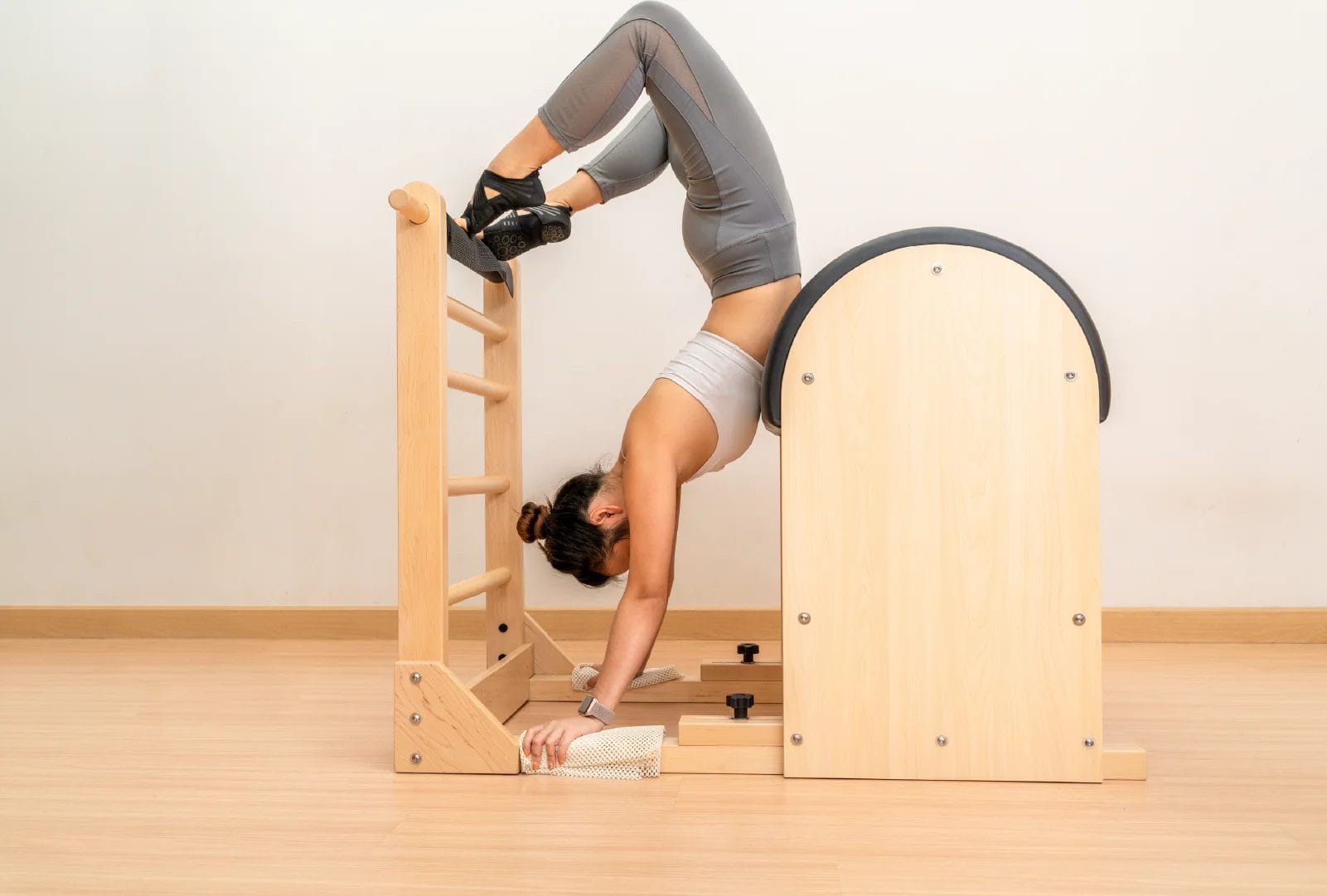 A Pilates instructor performs an advanced backbend using the Pilates Barrel apparatus.