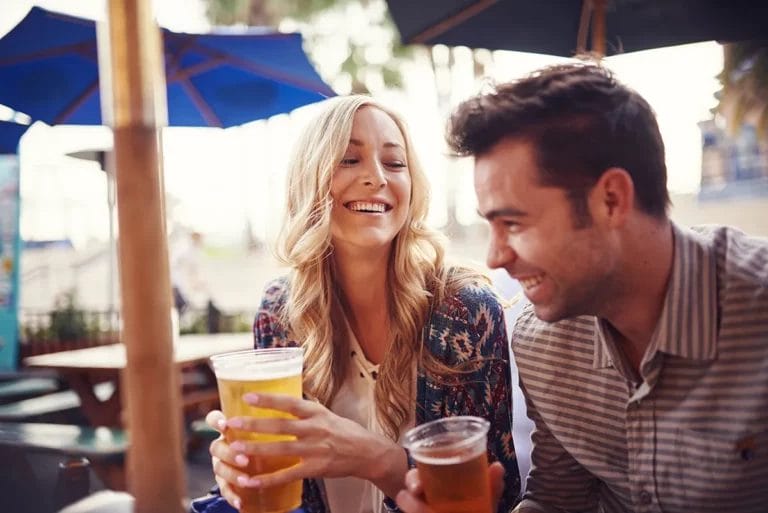 A woman and man smile while holding beer in plastic cups at an outdoor venue.