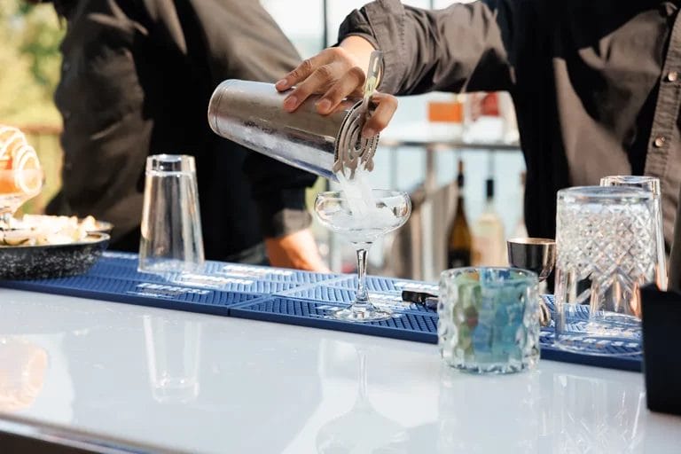 A close-up of a bartender pouring a cocktail into a glass at an outdoor bar.