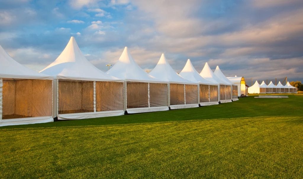 A row of empty white pop-up tents on an empty festival grounds at sunset.