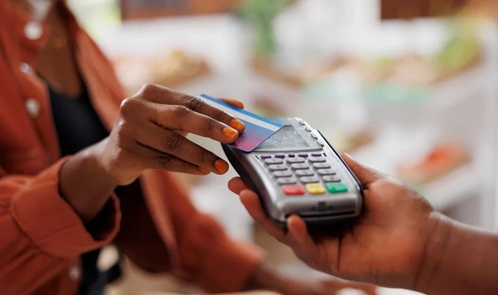 A close-up of a customer using credit card to make contactless payment for fresh organic produce at a local market.