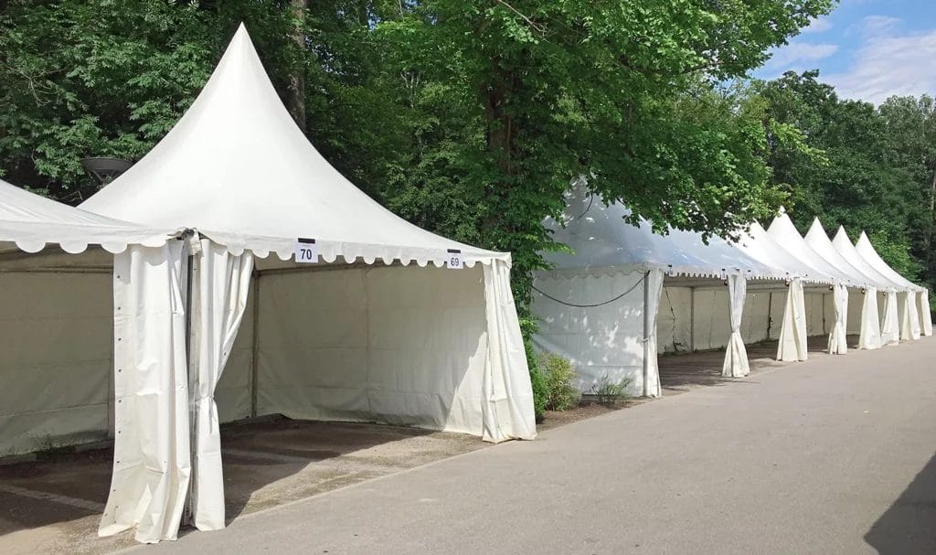 A row of empty vendor tents nestled between trees and foliage at an outdoor event.