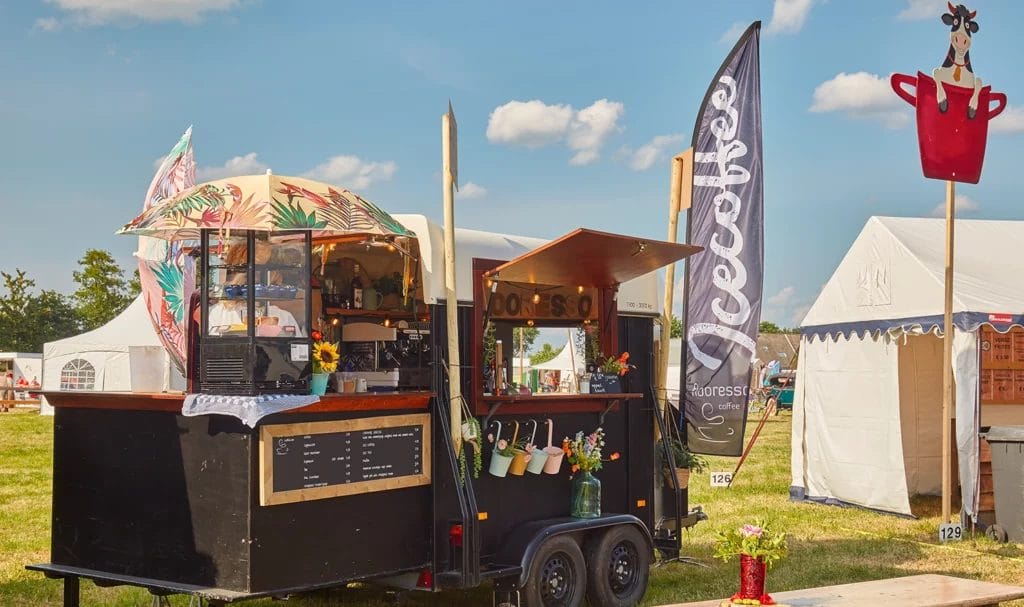 Decorative black food truck selling coffee drinks at an outdoor country fair.