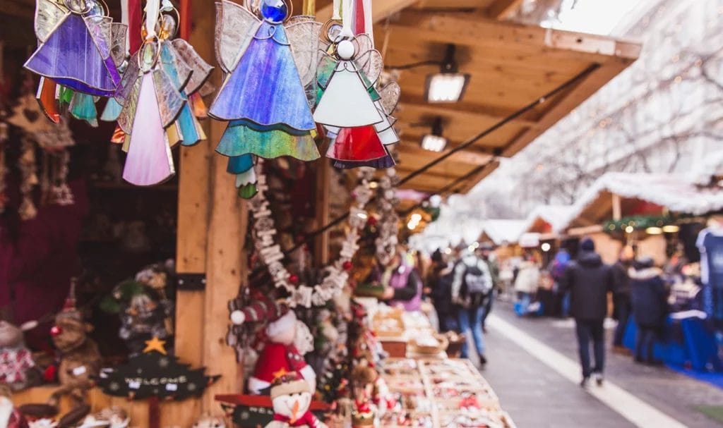 Art vendor kiosk with handmade Christmas decorations on display in an outdoor holiday market.