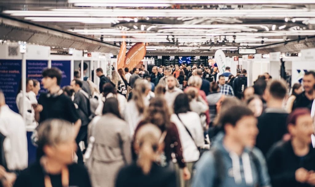 Blurred crowd of people at walking through a large, indoor exhibition hall amongst the booths at the trade show.
