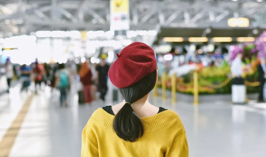 A woman in a red beret and yellow sweater looks out at a trade fair exhibition hall.