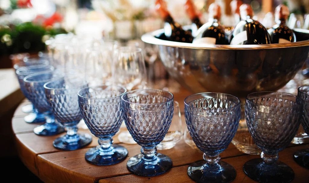 Close-up of a wooden table with blue, vintage-style glasses and a bowl of champagne bottles.