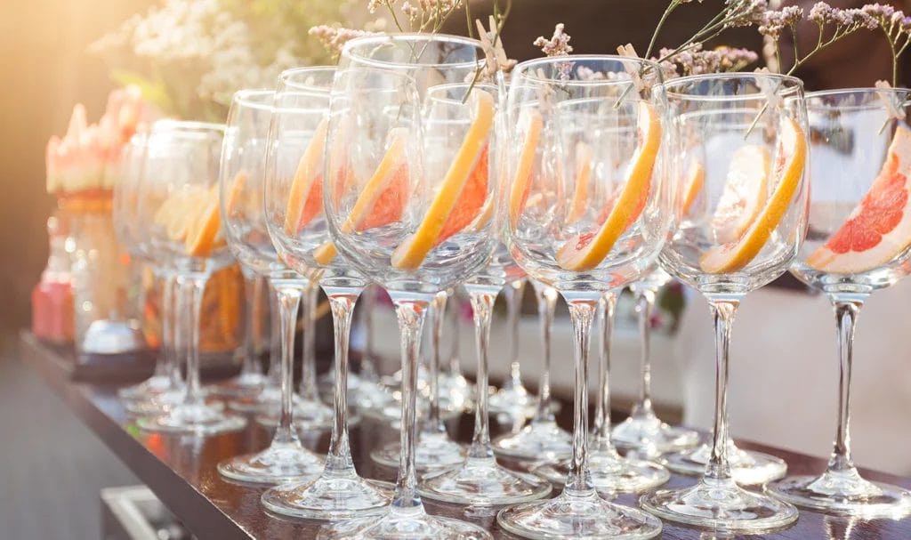 Slices of grapefruit and pieces of flowers sit in champagne glasses as part of a garnish for a custom cocktail at a wedding party.