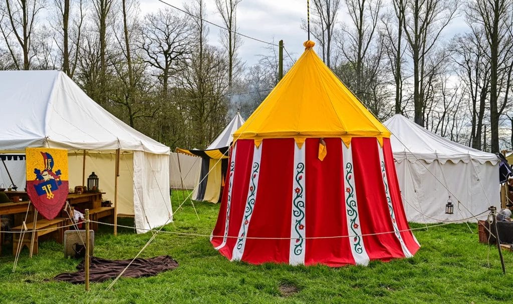 A medieval tent made of red, yellow, and white fabric is being used by a vendor at a medieval market.
