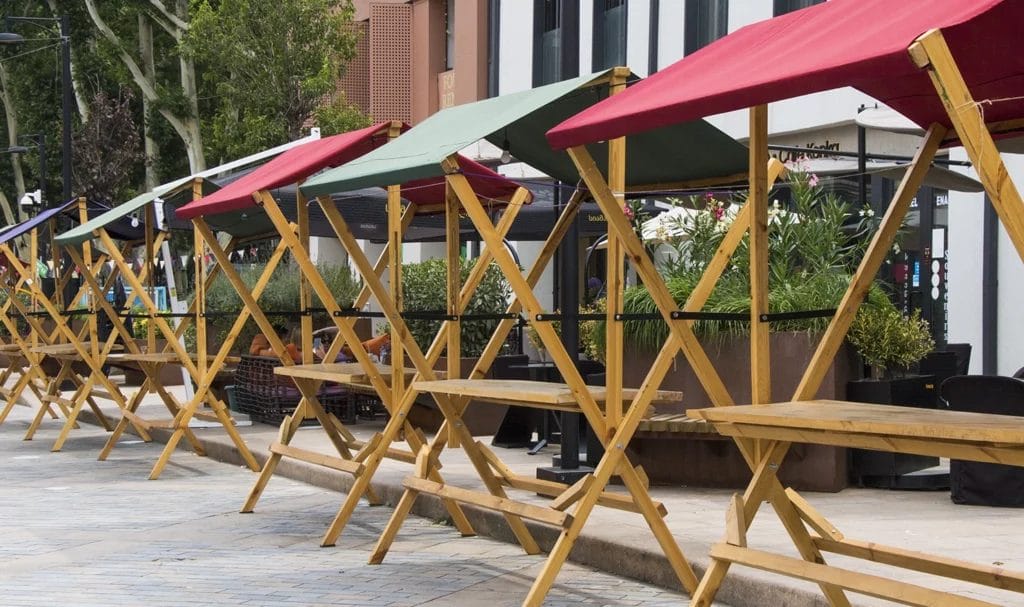 Empty wooden vendor tables with tents line an open-air marketplace before a festival.