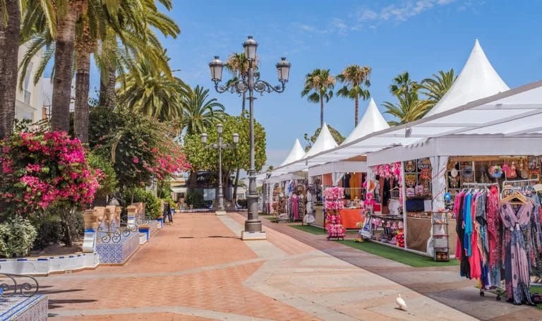 A row of white vendor tents sit in an outdoor city center for a market. The booths are selling clothes, sweets, and souvenirs.