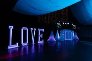 A blue and purple-lit wedding dance floor featuring large fluorescent letters spelling "love" and a DJ booth.