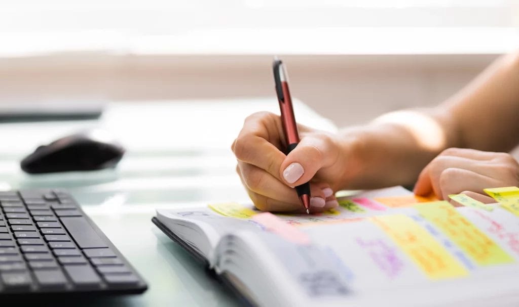 Close-up look at an event organizer writing in a planner full of colorful sticky notes and reminders.