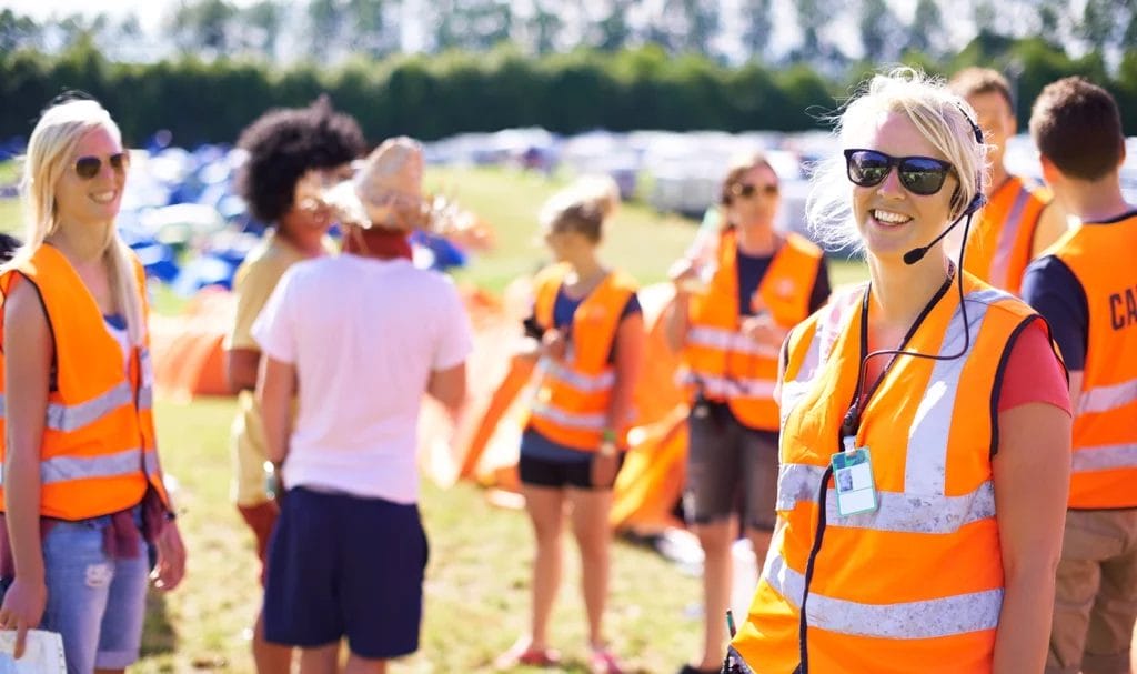 A group of event employees in bright orange safety vests are chatting and briefing before an event.