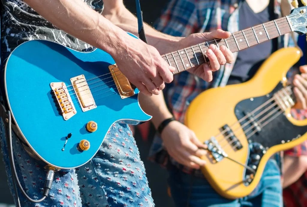 A zoomed-in photo of two guitarists playing their instruments on an outdoor stage.