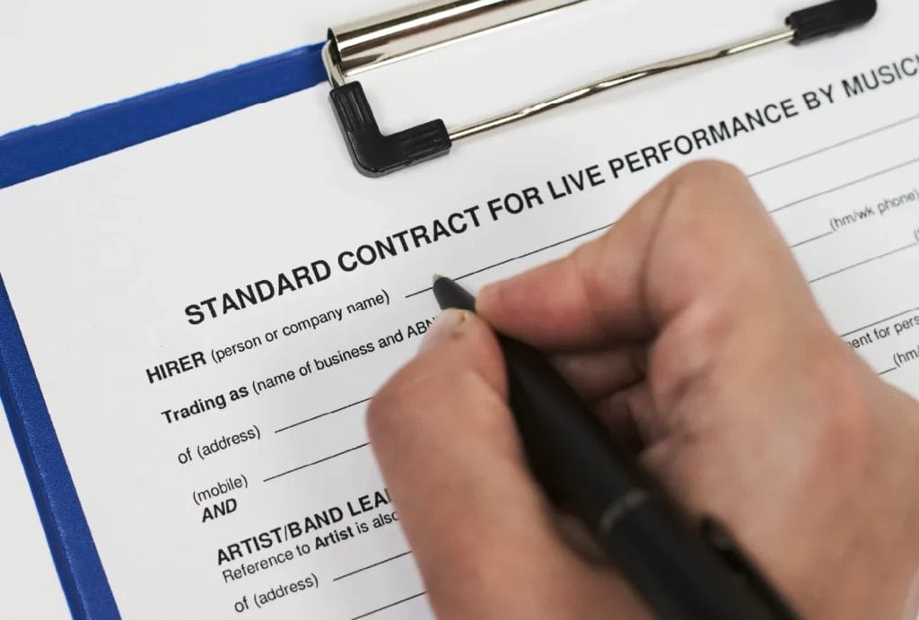 Close up of a hand signing a contract that reads "standard contract for live performance by musician.