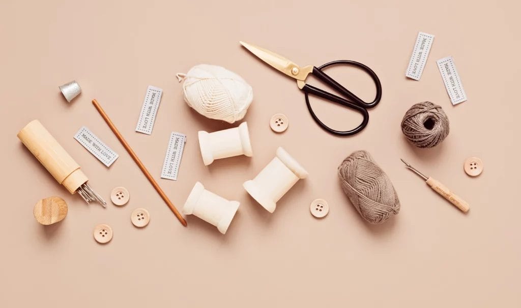 Sewing supplies and tools for needlework are scattered across a beige background.