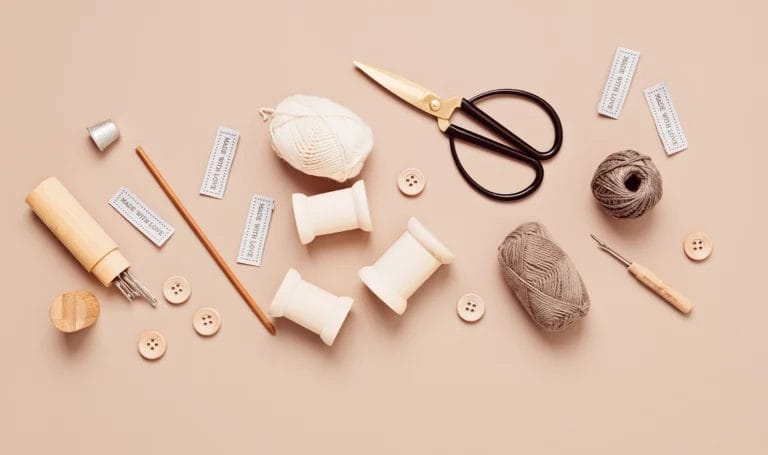 Sewing supplies and tools for needlework are scattered across a beige background.