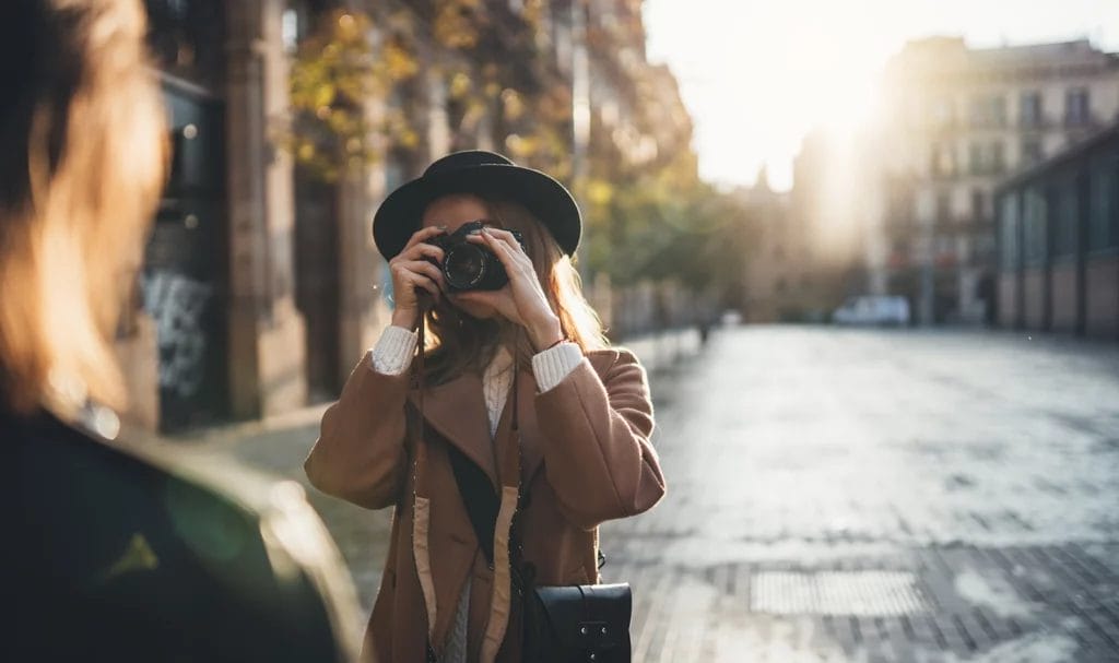 Young woman with a camera has her friend pose on an empty cobblestone street for a picture with a digital camera.