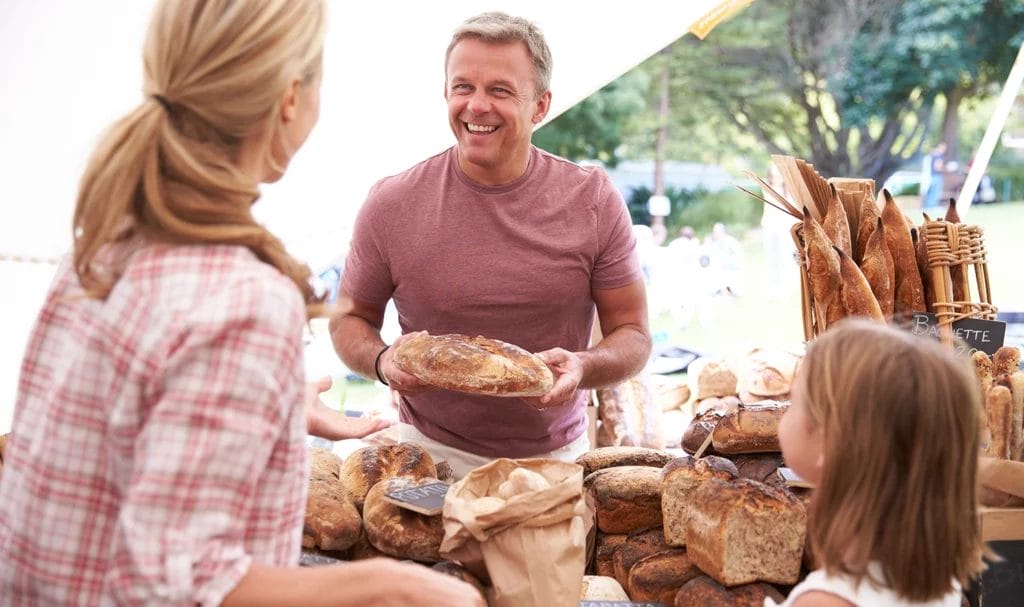 Family buying bread from a bakery stall at a farmers market.