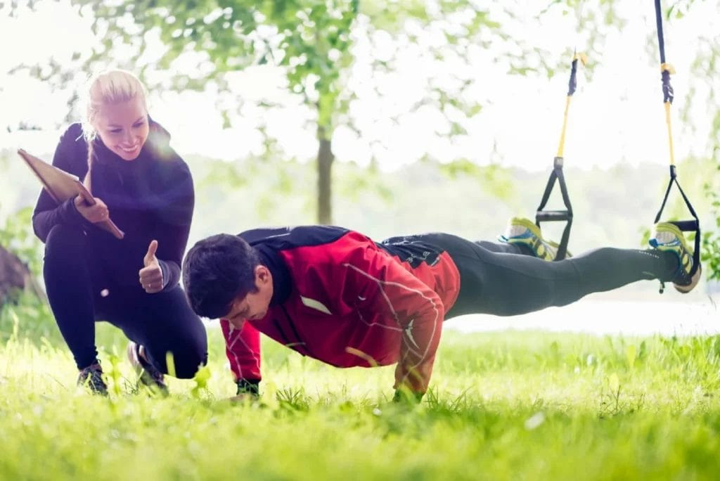 Personal trainer encouraging client to do pushups outside with ankle harnesses