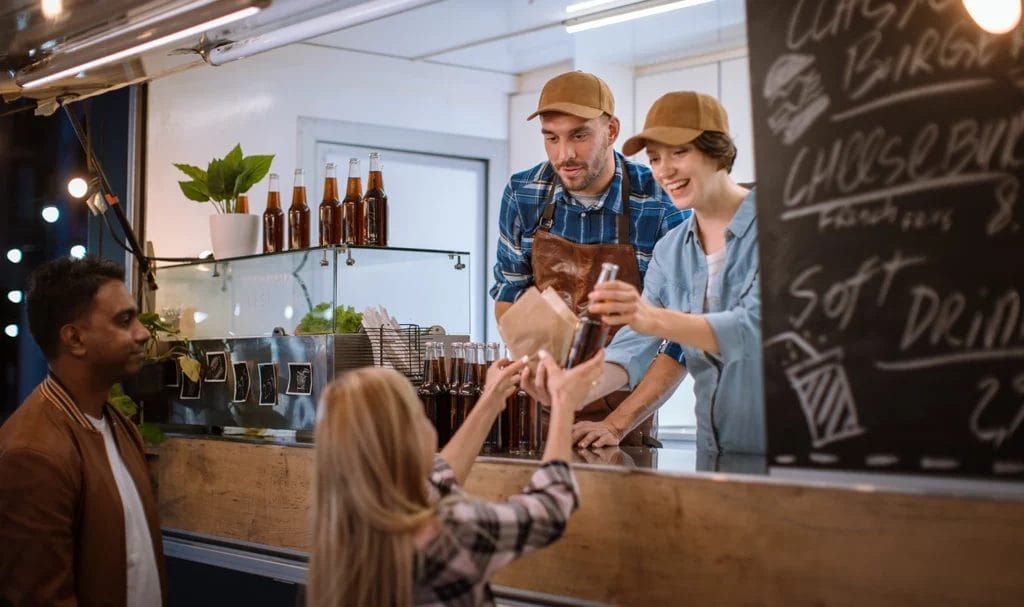 Food truck employees hand out a burger and cold drink to a happy young customer.