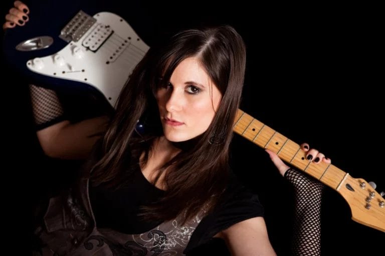 Woman holding an electric guitar behind her head.