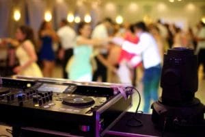 A wedding DJ booth in front of a dancing crowd.