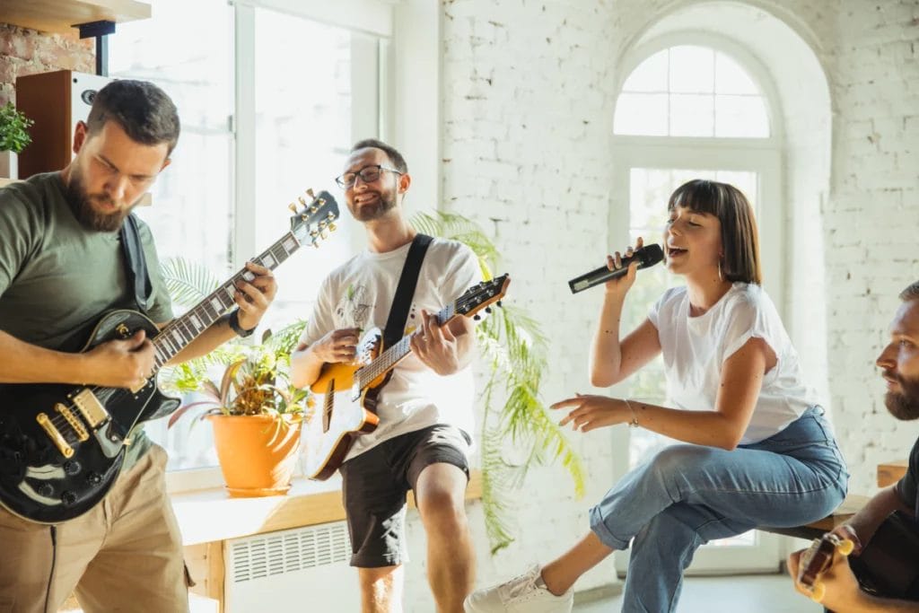 A casual music group featuring a singer and two guitarists rehearsing in a bright room with white brick walls.