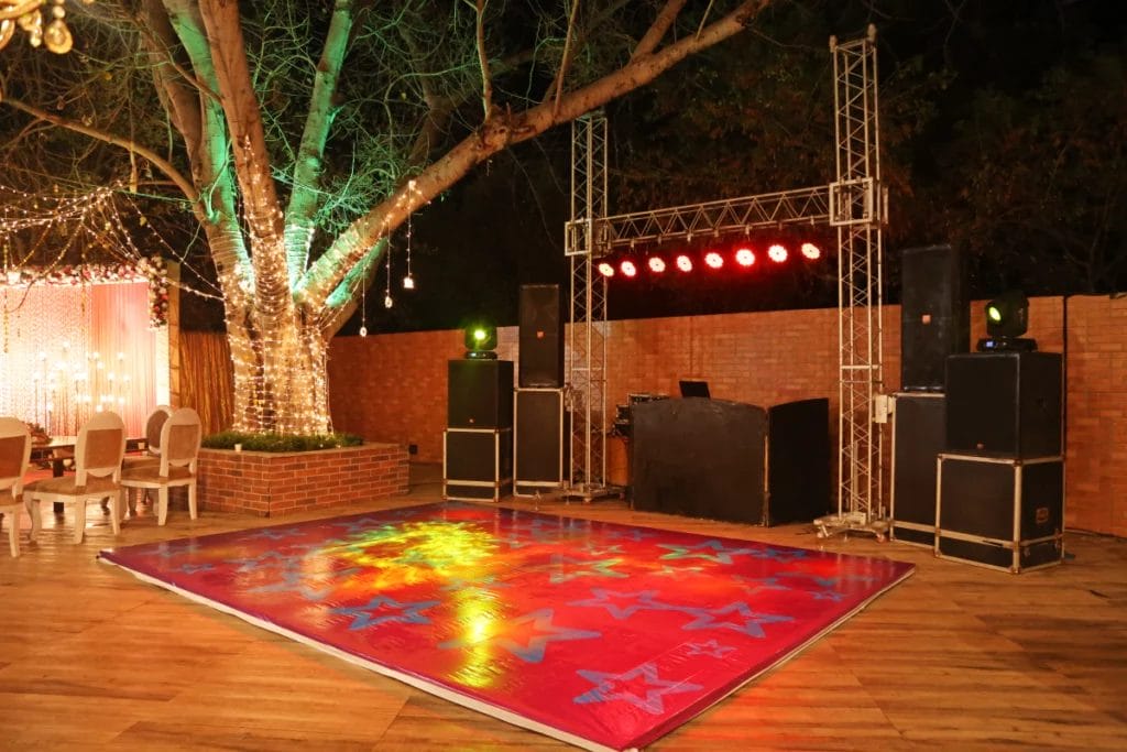 An outdoor wedding dance floor and DJ setup featuring a red floor and red lights.
