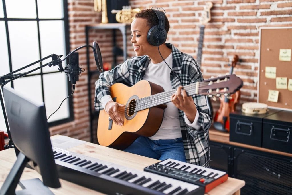 Musician with short hair playing acoustic guitar while singing into a mic in a recording studio.