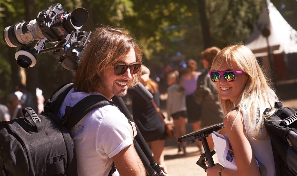 Videographer and photographer walking through a crowd at an outdoor event, taking a moment to smile for a photo.