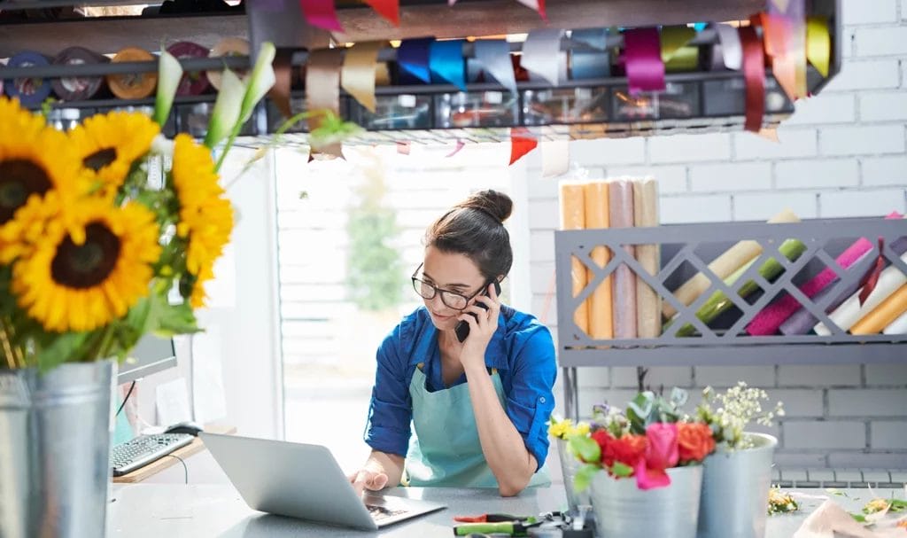 Female businesswoman talking on the phone while using a laptop inside of a craft studio.