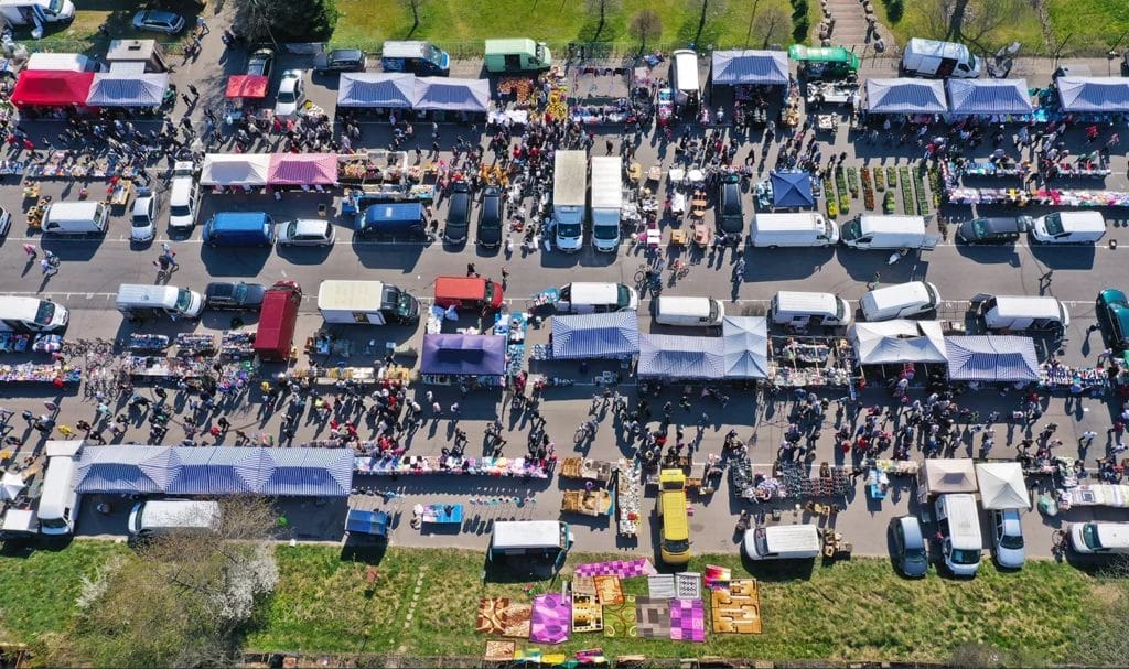 Aerial view on flea market with tents, booths, and food trucks amongst crowds of buyers and sellers.