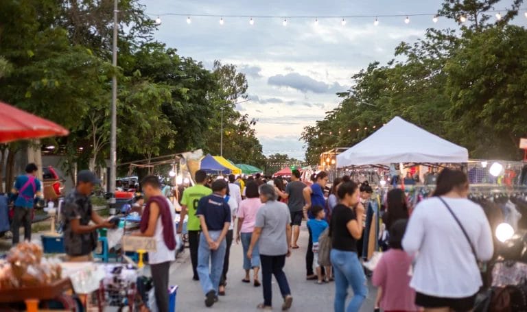 Looking down the pathway of an outdoor market in the evening. The walkway is lined on either side with food vendors and booths selling handmade goods.