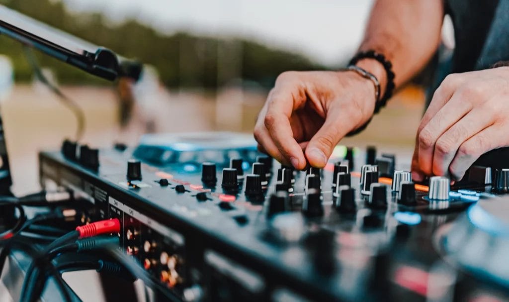 Close-up look at a DJ's hands creating and regulating music on a console mixer at an outdoor event.