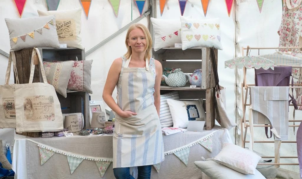 A craft vendor poses in her booth next to her display of handcrafted homegoods.