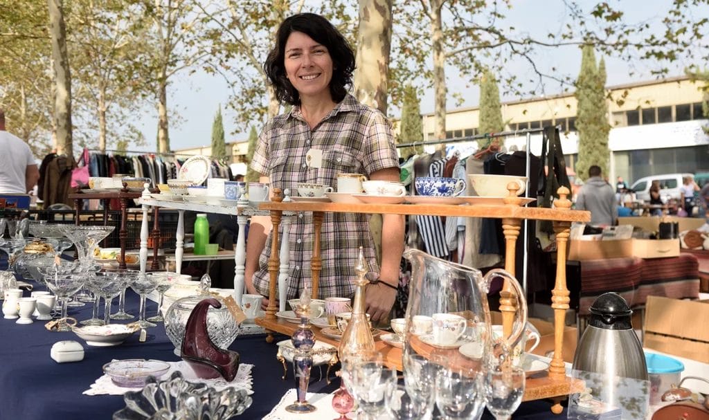 Woman smiles for a photo with her booth setup full of home decor and vintage items at a flea market shop.