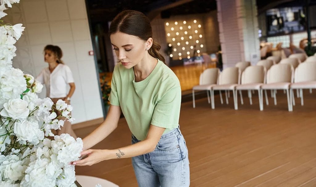 A florist secures white flowers in place to a display at the front of a banquet hall.
