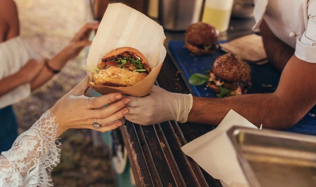 Close-up look of a food truck vendor passing a turkey burger to a customer.